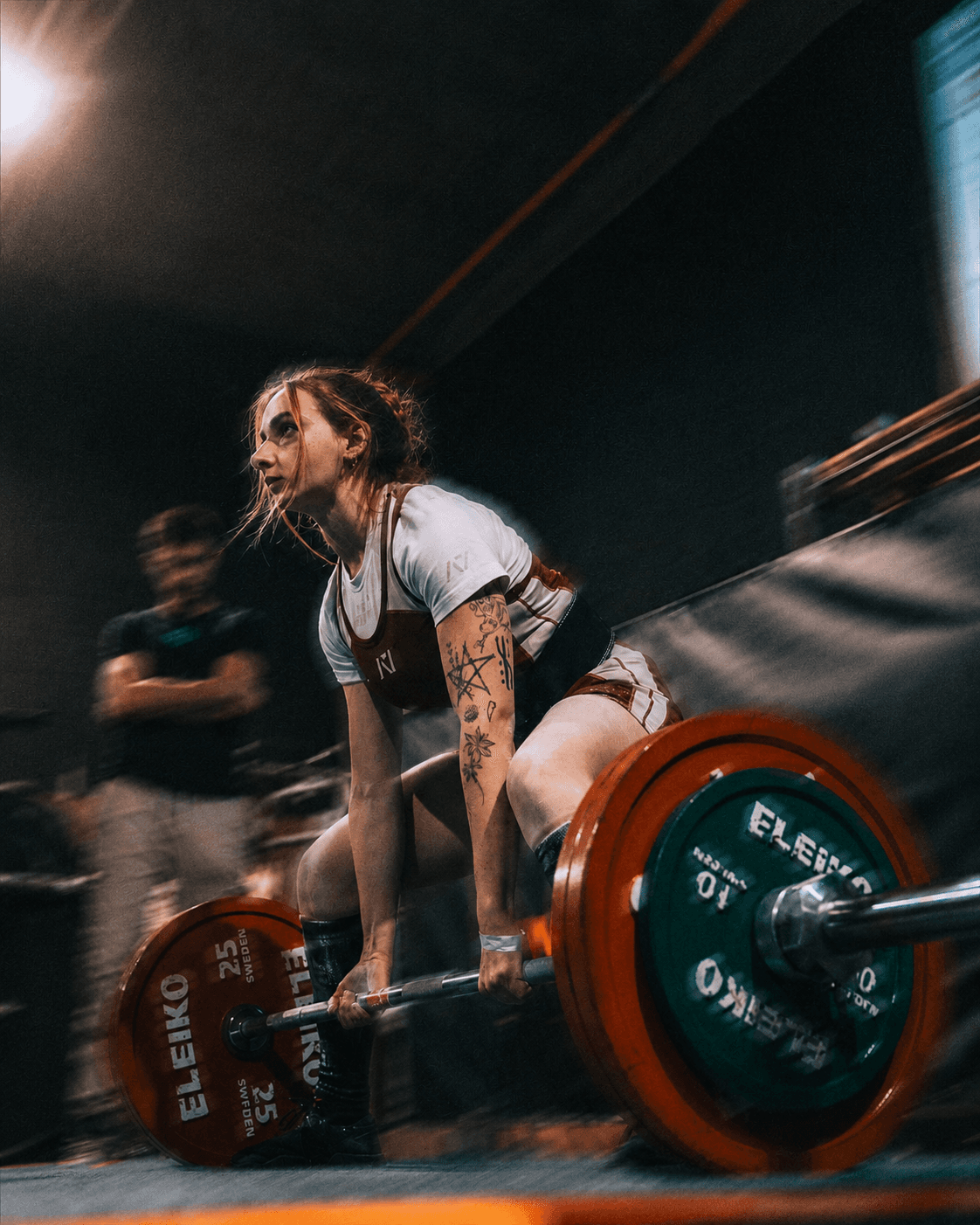 Atleta de powerlifting levantando una barra durante una competencia, con su entrenador observando